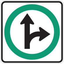 Sign with a split arrow in side of a green circle. One of the arrows points straight forward and the other curves to the right. This sign indicates that drivers must either go straight or turn right.