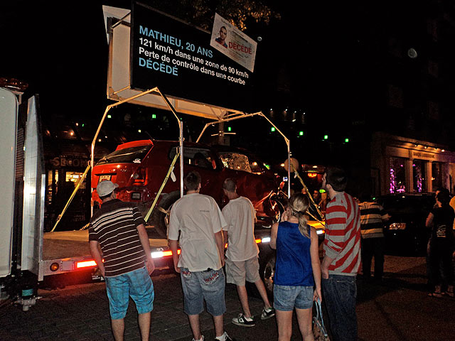 Photo of people in front of an accident-damaged vehicle taken during the field operation in front of the Loews Le Concorde hotel, in the city of Québec